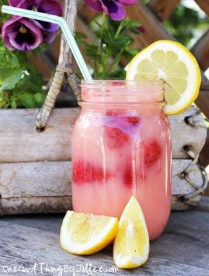 a mason jar filled with lemon and raspberry punch next to flowers on a wooden table