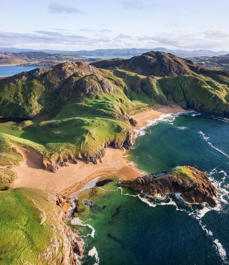 an aerial view of the ocean and coastline with green hills in the background, along with blue water