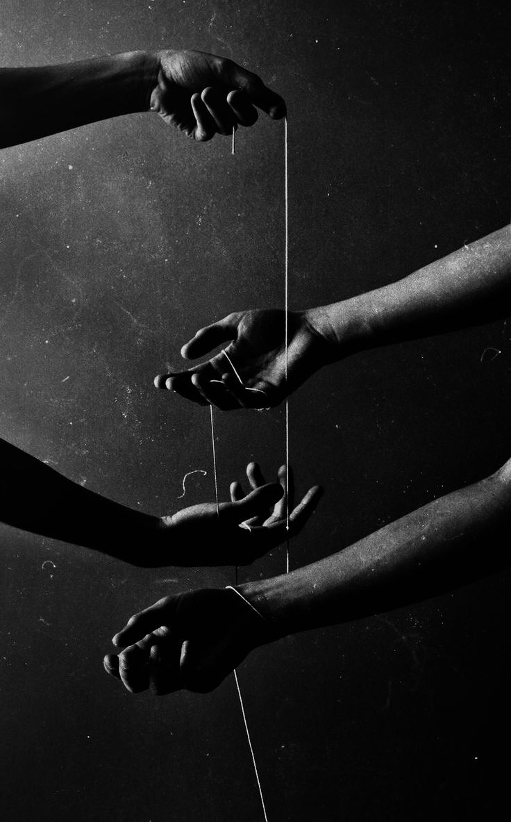 four hands reaching for something with string attached to it in black and white photo, against dark background