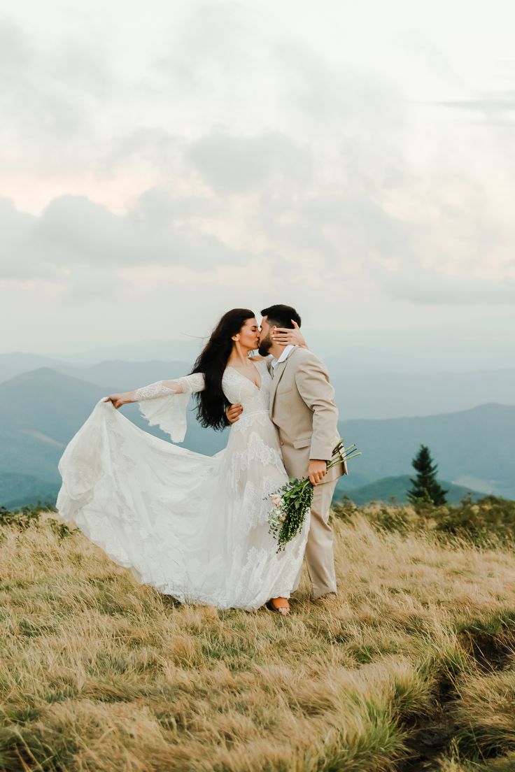 a bride and groom standing on top of a grass covered hill