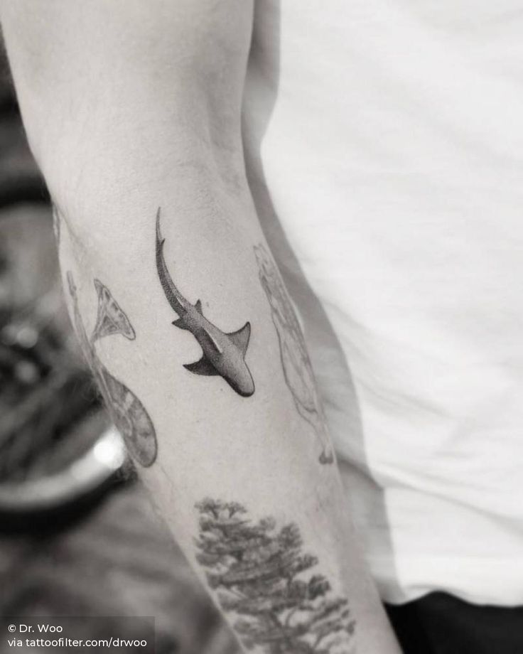 a man with a tattoo on his arm has a shark and trees in the background