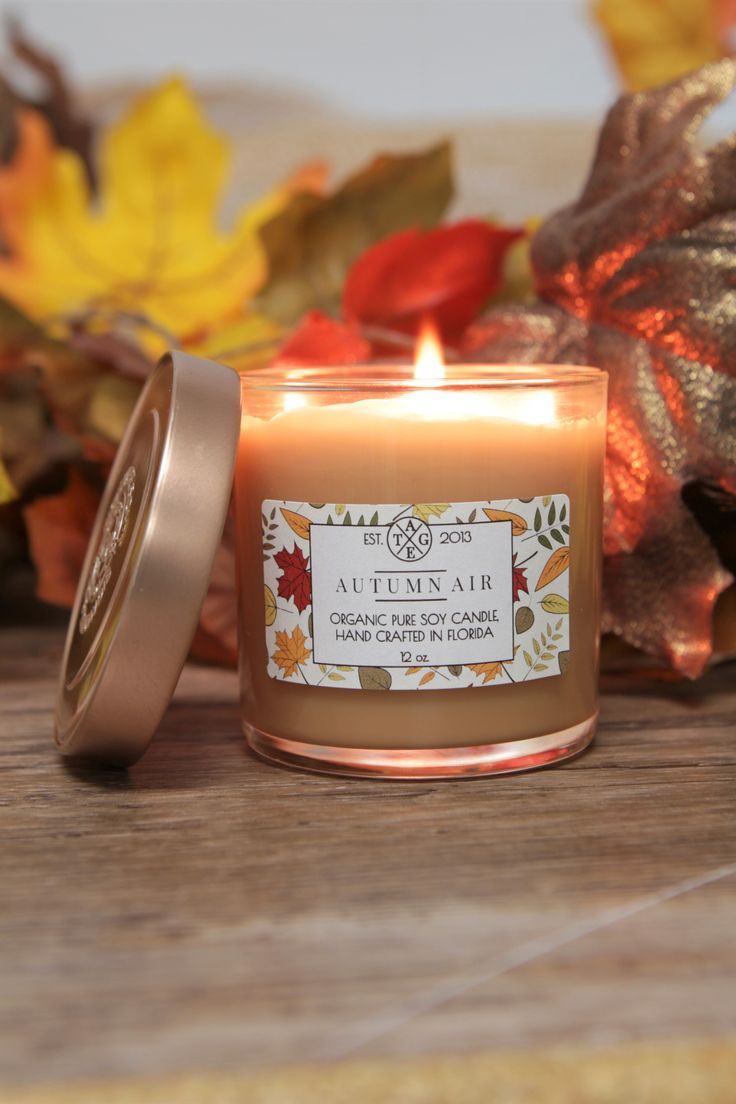 a candle sitting on top of a wooden table next to leaves and fall foliages