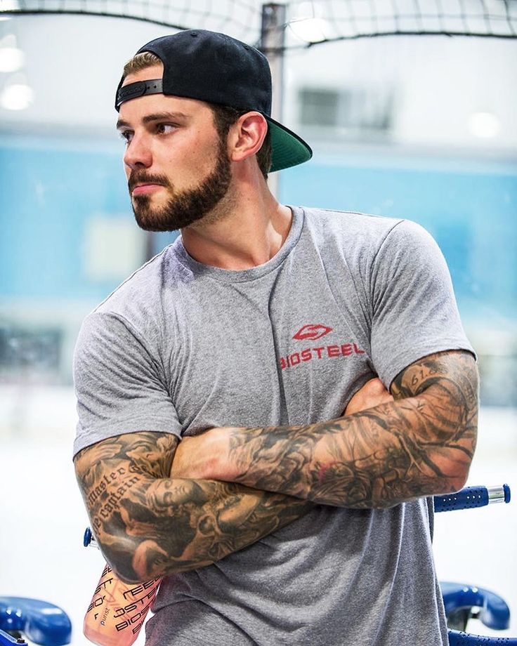 a man with tattoos on his arm and arms crossed, standing in front of a gym