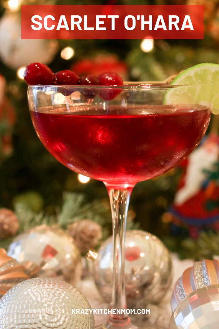 a close up of a wine glass with a drink in front of a christmas tree