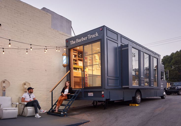 a man and woman sitting on the steps of a tiny house that is built into the side of a building