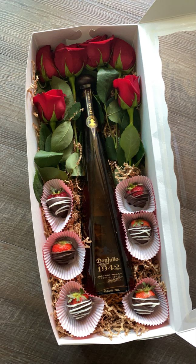 a bottle of wine and some chocolates in a box with roses on the table