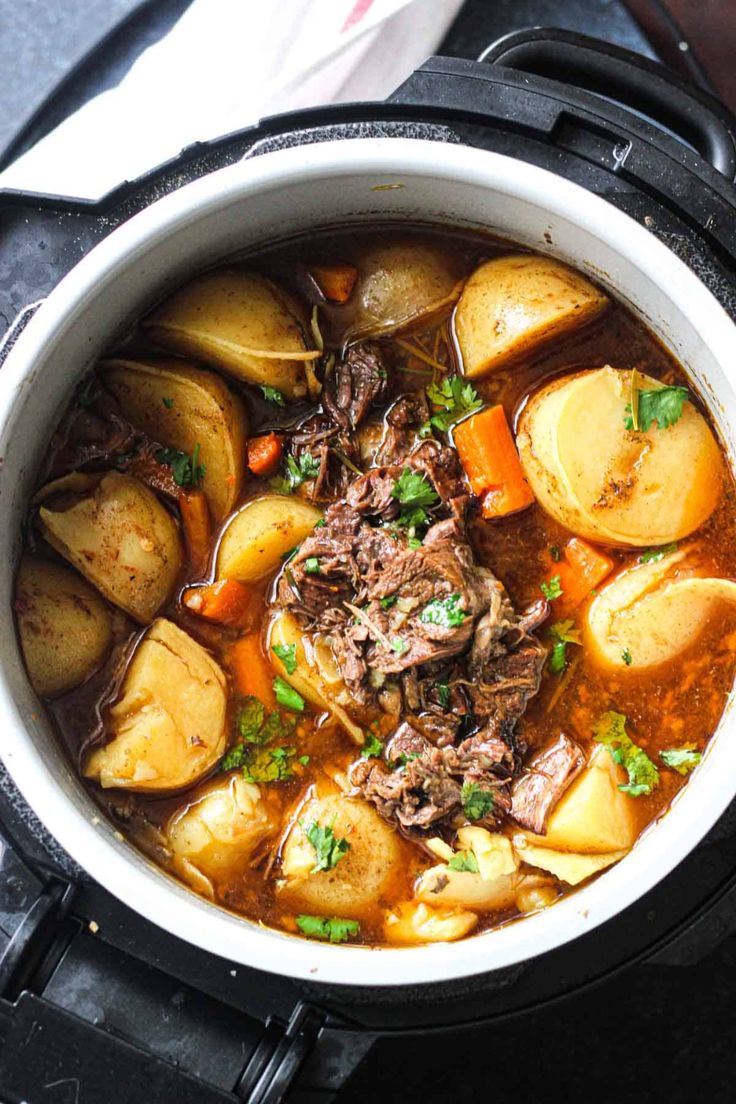 a pot filled with beef and potatoes on top of a stove burner next to a napkin