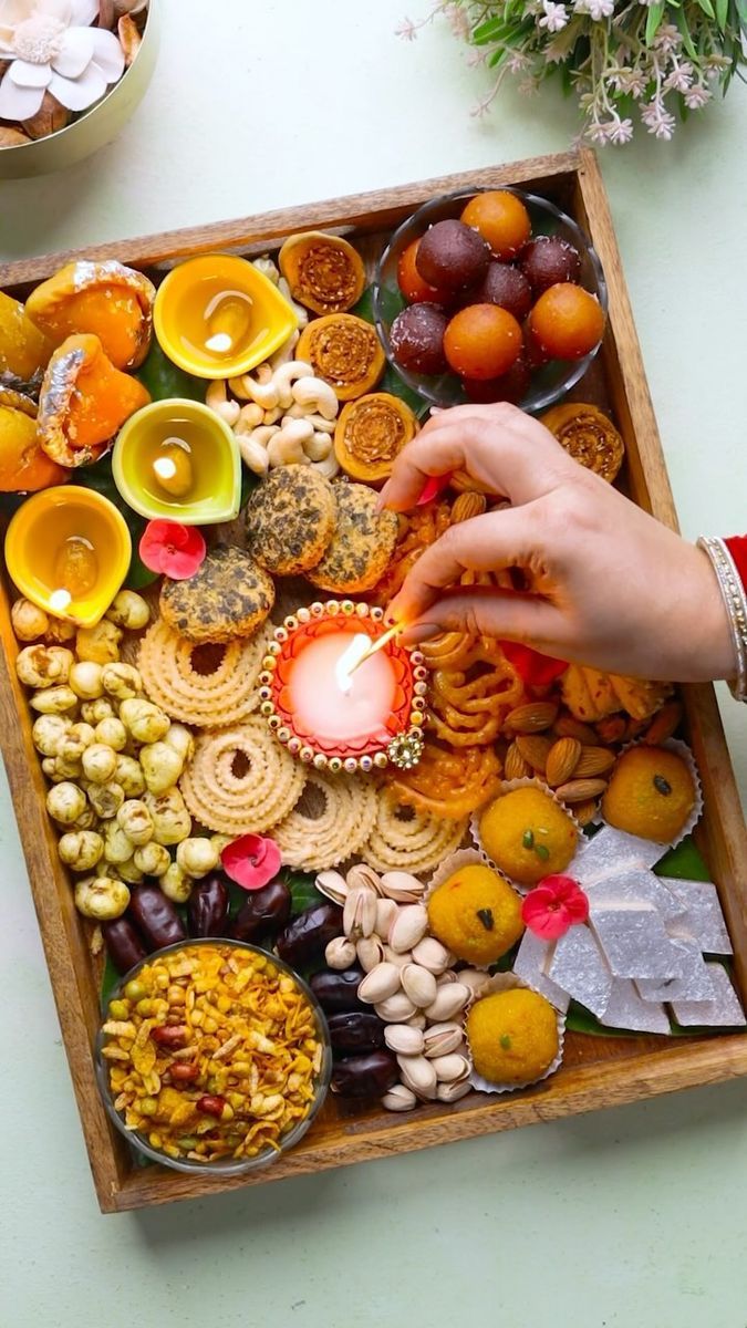 a wooden tray filled with assorted food and a hand reaching for a lit candle