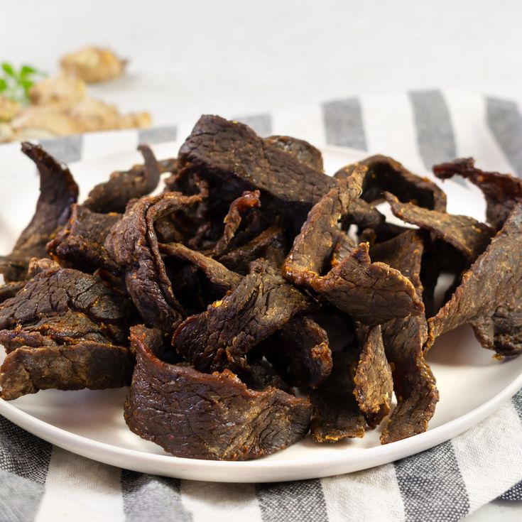 a white plate topped with beef strips on top of a table