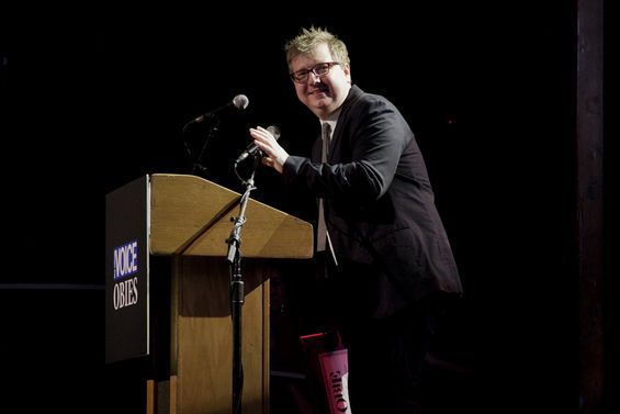 a man standing at a podium with a microphone in front of him and holding his hand out