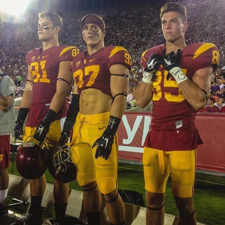 two football players standing next to each other in uniforms on the sidelines at a game