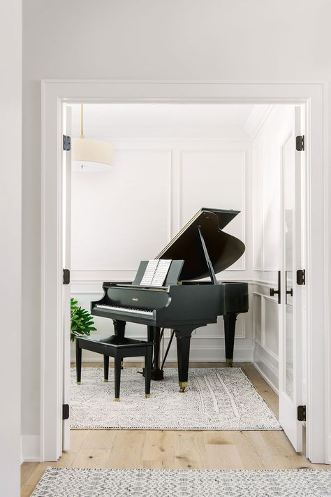 a grand piano sits in the entryway of a white house with wood floors and walls