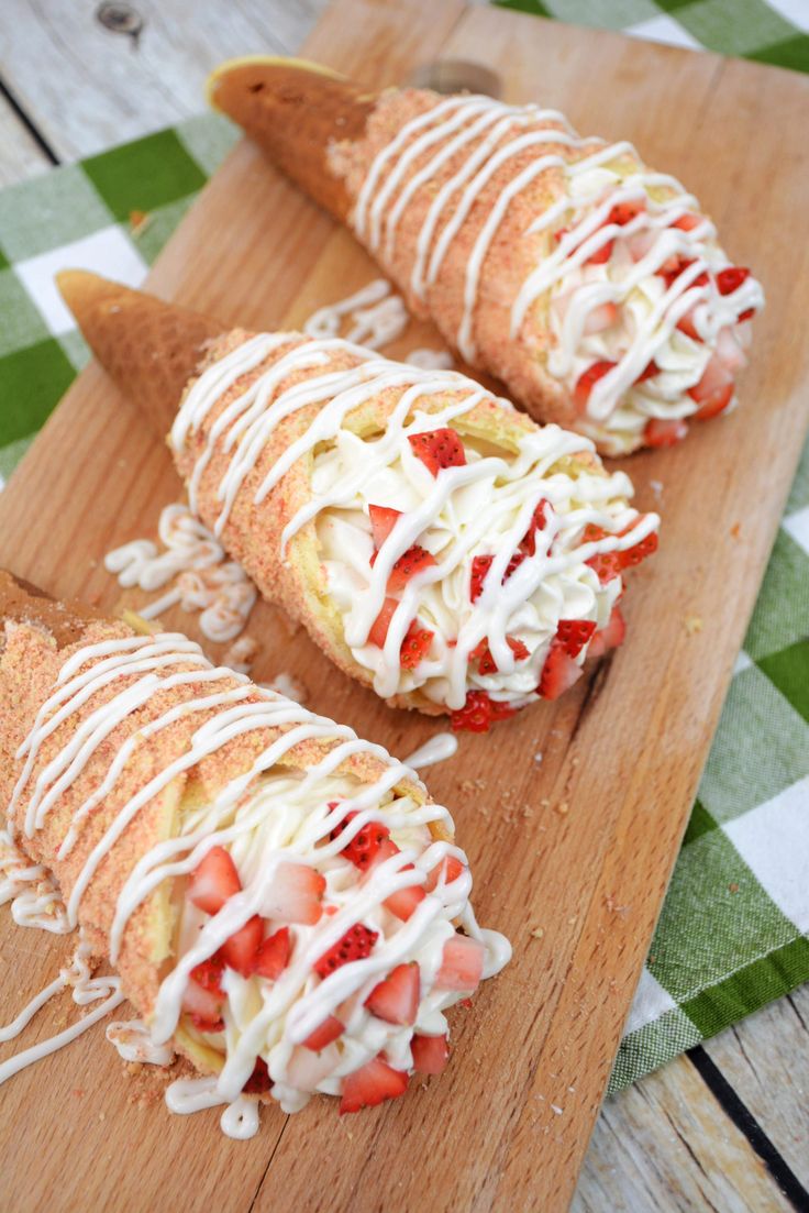 three pastries with strawberries and cream drizzled on them sitting on a cutting board