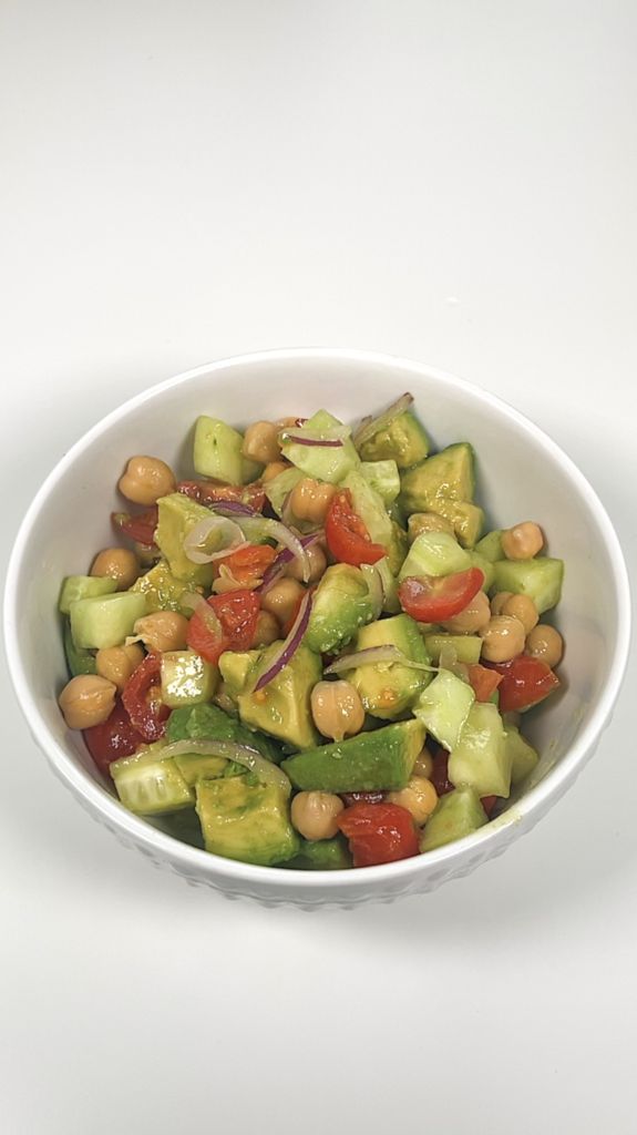 a white bowl filled with cucumber, tomatoes and chickpeas on top of a table