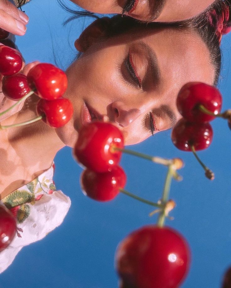 two women with their eyes closed and one has her face close to the cherries