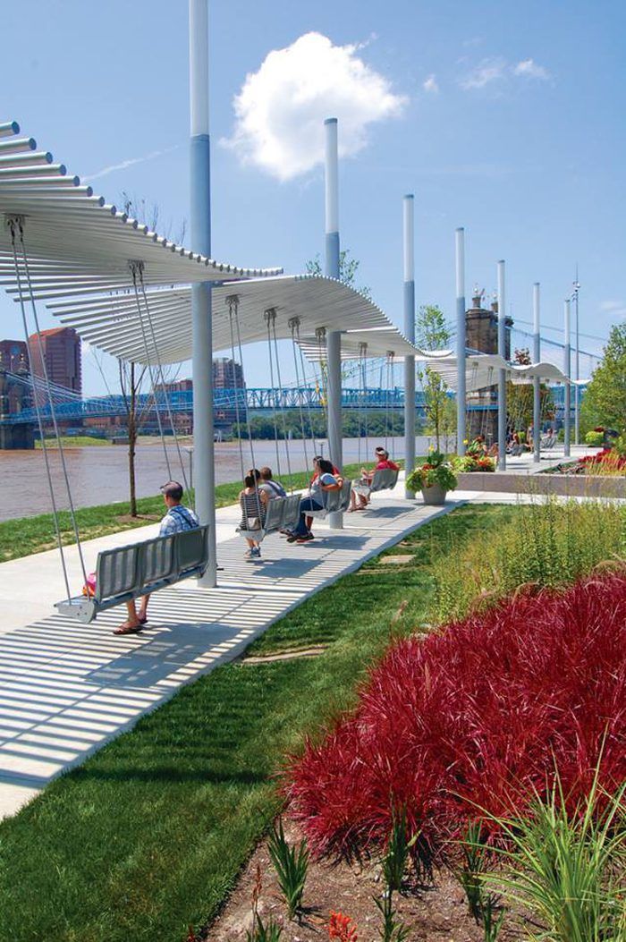 people sitting on benches under an awning in a park with red flowers and green grass