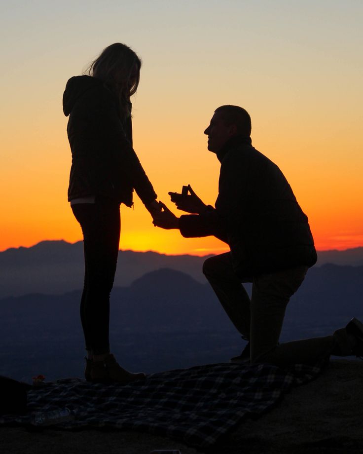 two people standing on top of a mountain at sunset