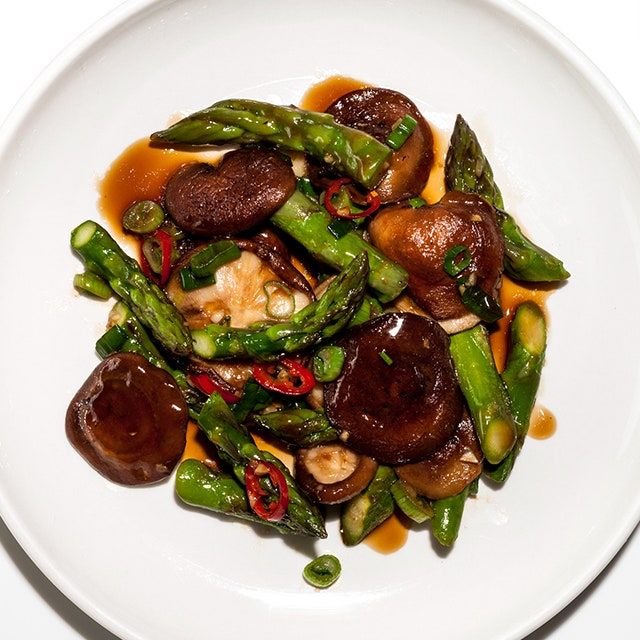 a white plate topped with asparagus and mushrooms covered in sauce on top of a table