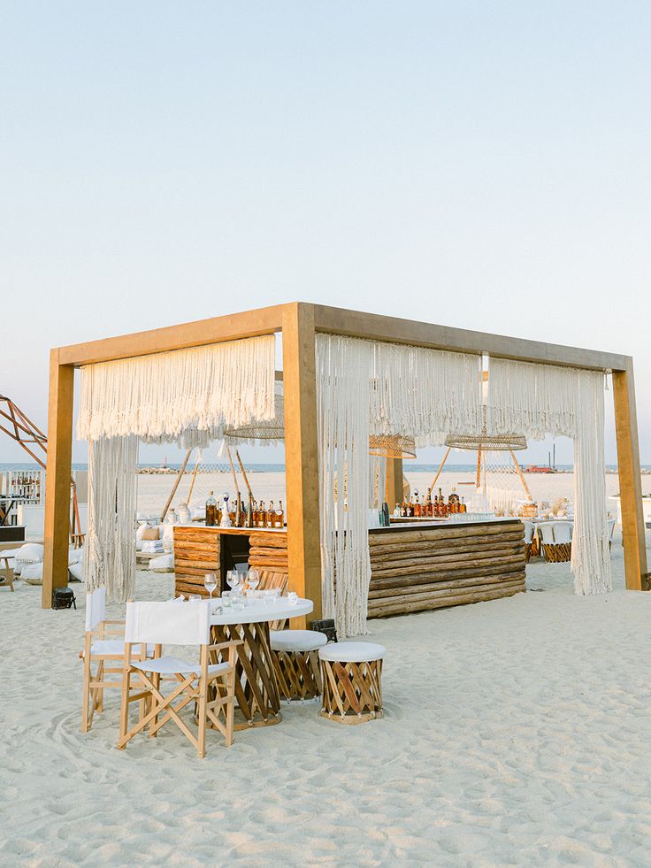 an outdoor bar set up on the beach with white chairs and tables in front of it