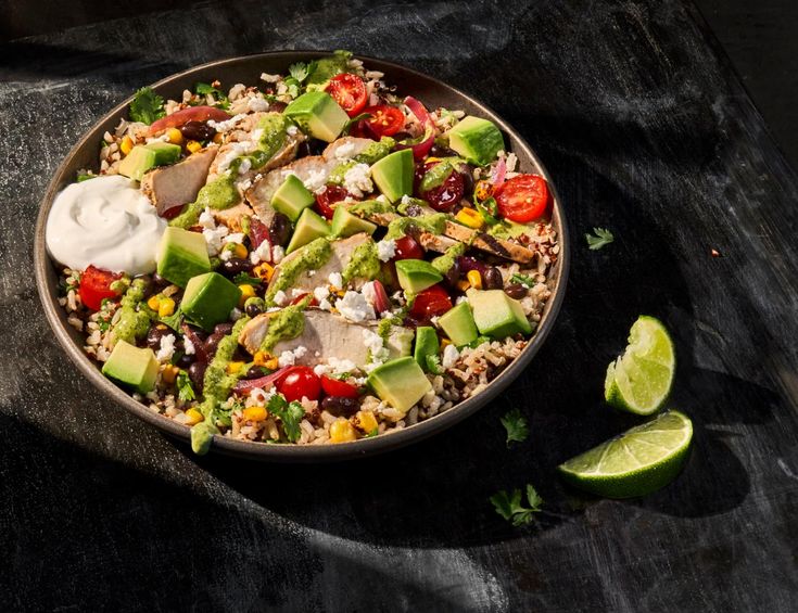 a bowl filled with rice, avocado, tomatoes, corn and sour cream