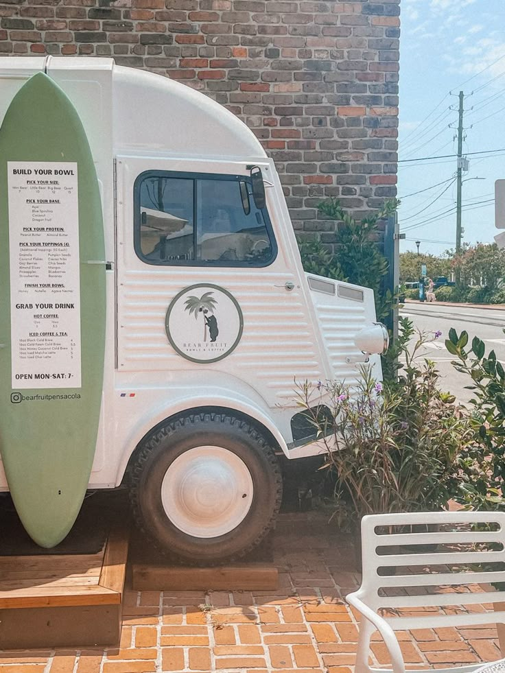 a surfboard is attached to the side of a food truck parked in front of a brick building