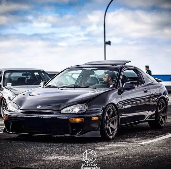 two cars parked next to each other in a parking lot with cloudy skies behind them