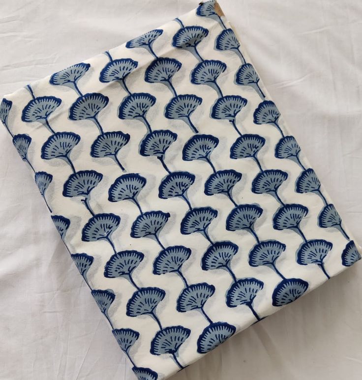 a folded blue and white cloth with fan designs on it, laying on a bed