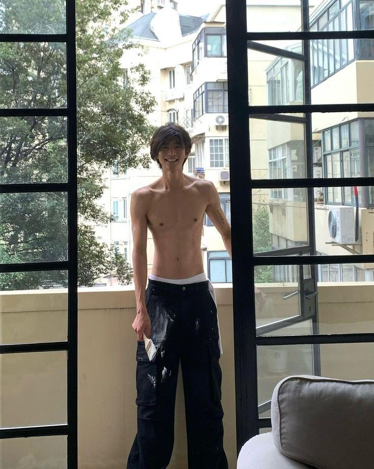 a shirtless man standing in front of a window