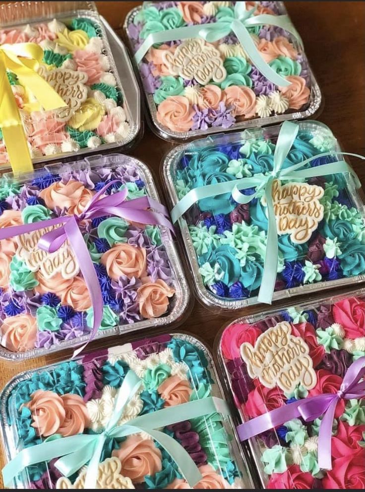 four plastic trays filled with different types of cupcakes and ribbons on top of a wooden table