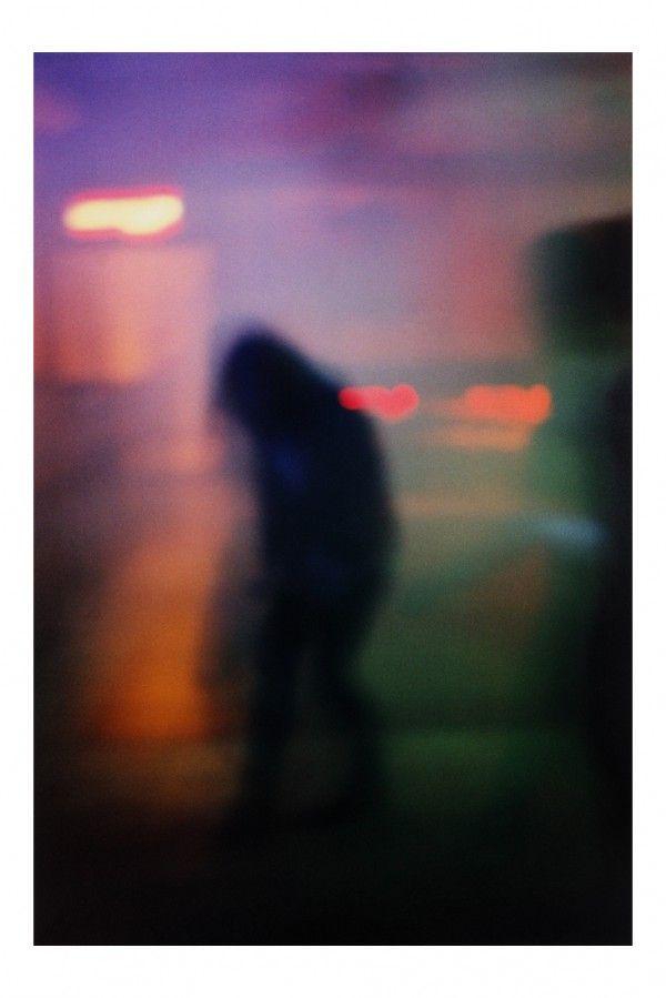 blurry photograph of person walking on sidewalk at night with city lights in the background