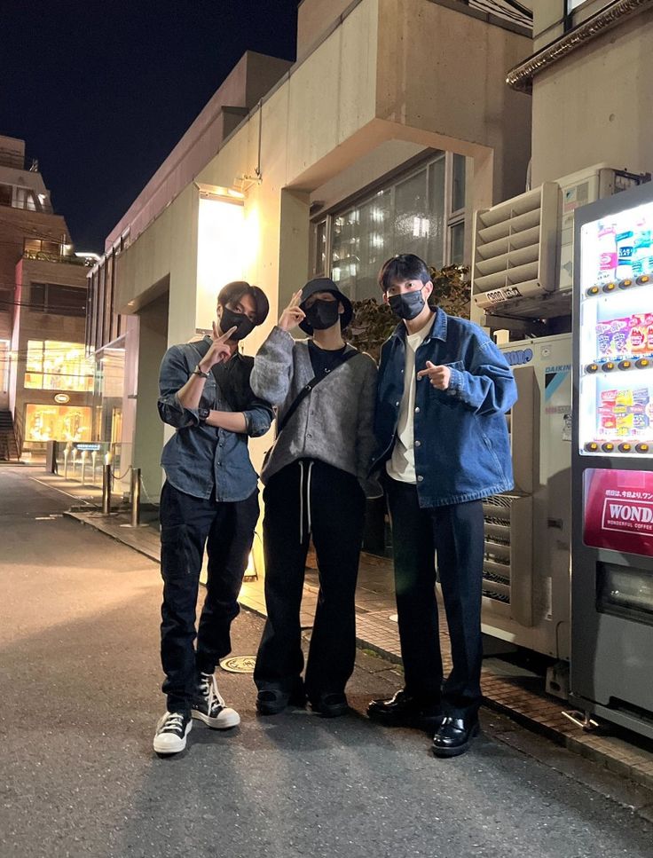 three men standing next to each other in front of a vending machine at night