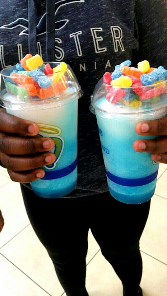 two people holding up cups filled with gummy bears and jellybe land milkshakes