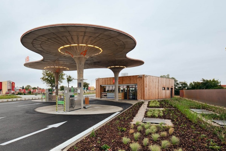 an empty parking lot with a gas station in the background and plants growing on the ground