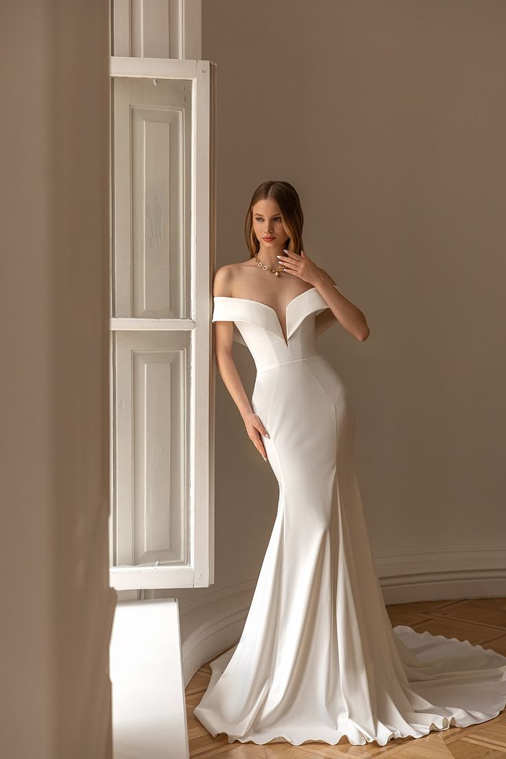 a woman in a white dress standing next to a window