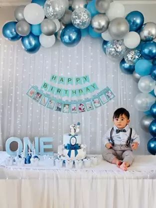 a little boy sitting on top of a table next to a cake and balloon arch