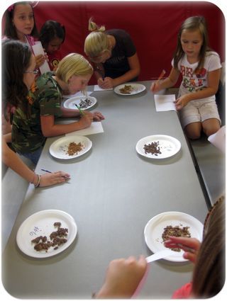 a group of children sitting at a table eating food from plates on paper plates with writing on them