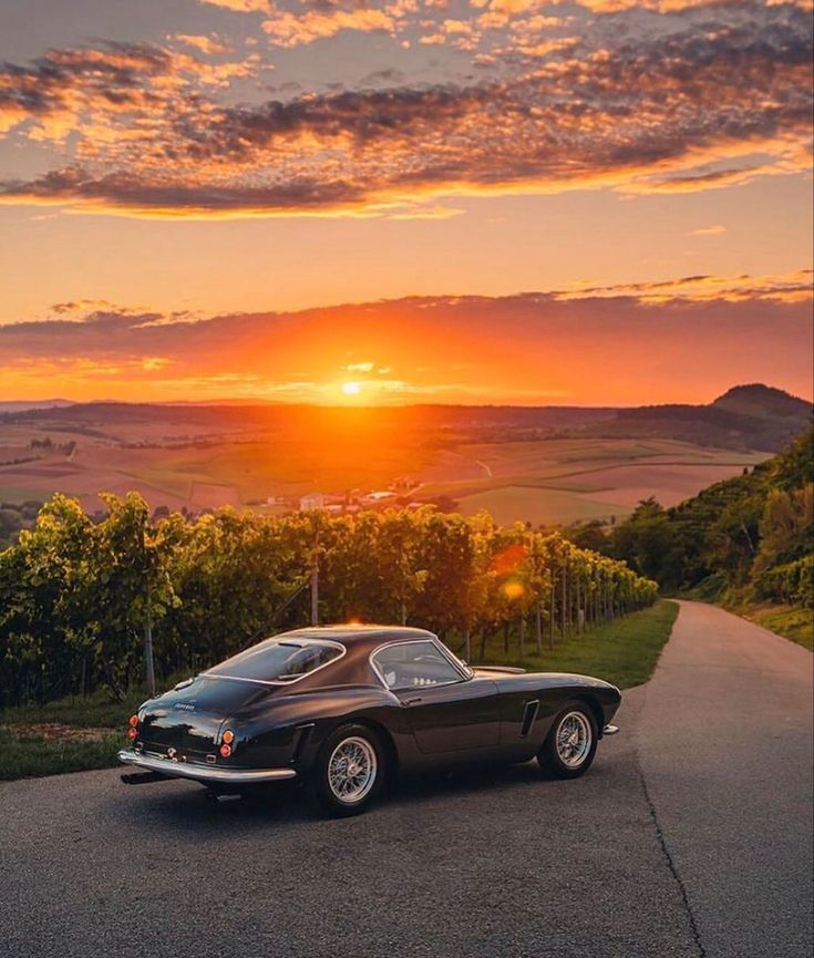 a black car parked on the side of a road at sunset with mountains in the background