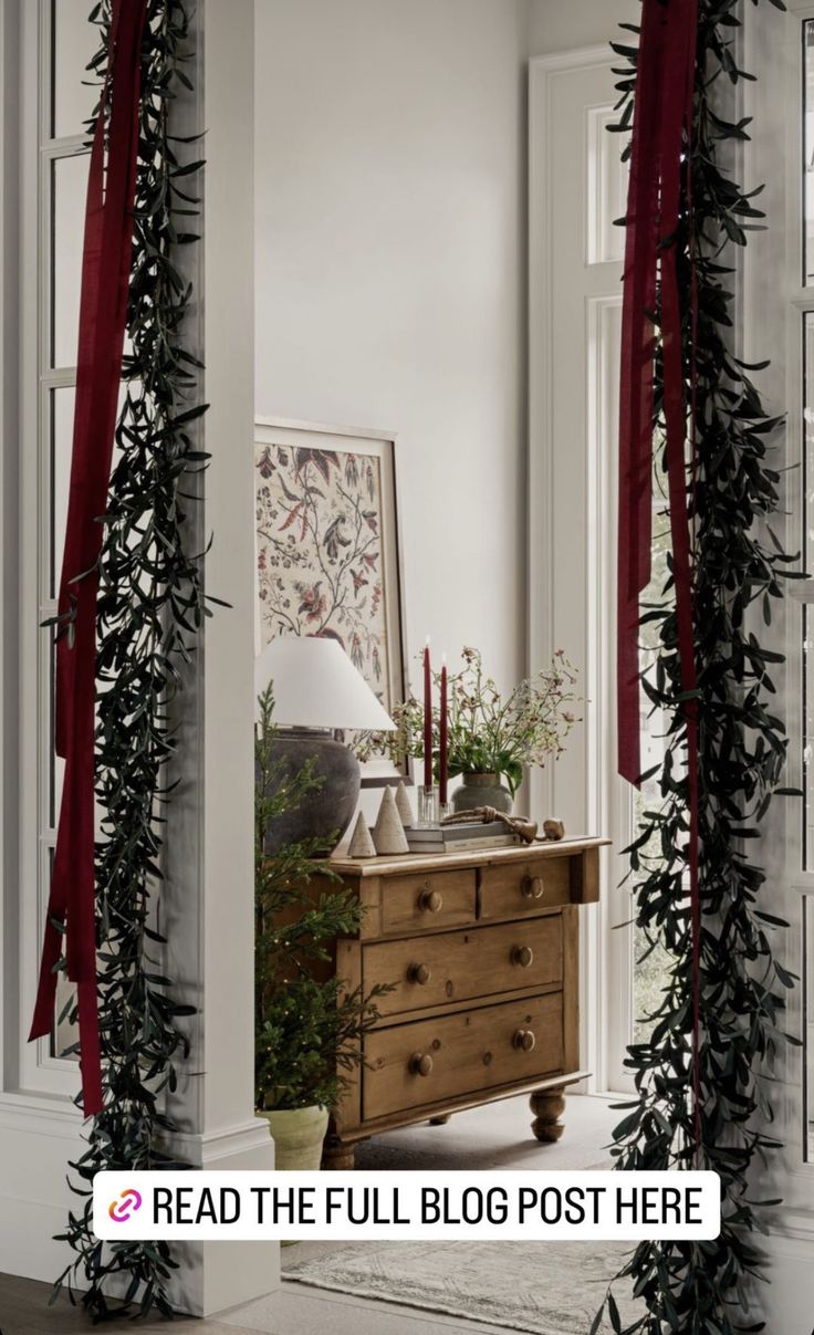 an old dresser is decorated with red ribbon and greenery for the holiday season in this white room