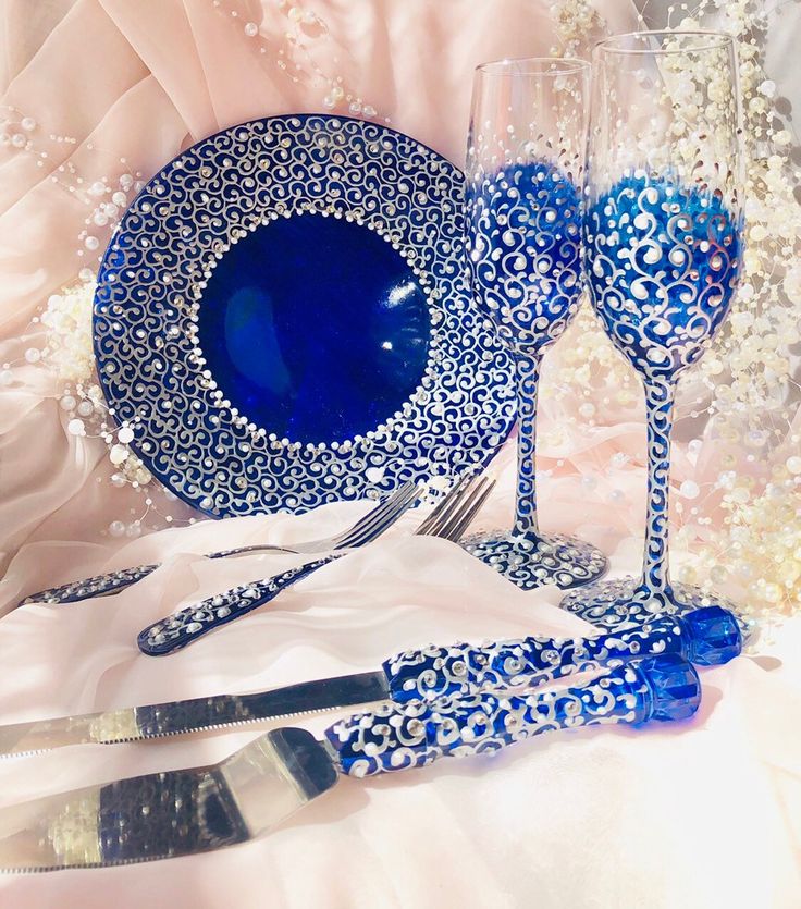 a blue and white table setting with utensils, wine glasses and silverware