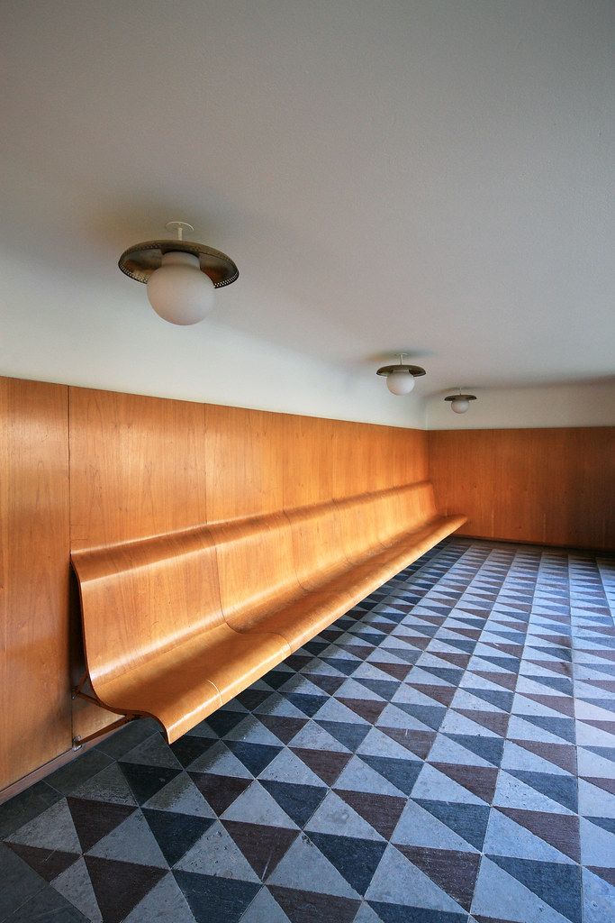 a long wooden bench sitting in the middle of a room with geometric carpet and wood paneling