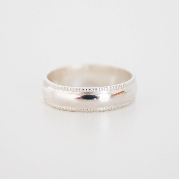 a white gold wedding ring with beaded edges on a plain surface, ready to be worn