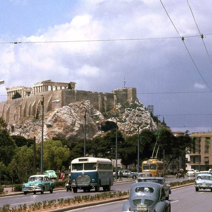 cars driving down the road in front of an ancient building