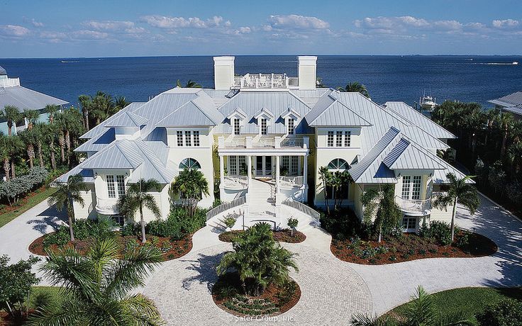 an aerial view of a large white house with palm trees and water in the background