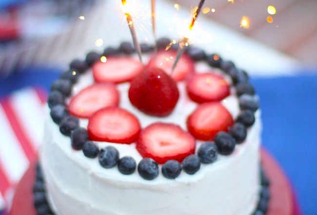 a white cake with strawberries and blueberries on top is topped with sparklers