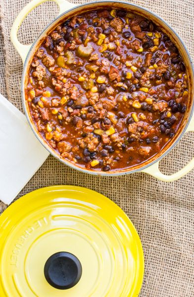 a yellow pot filled with chili and corn next to a yellow lid on a table