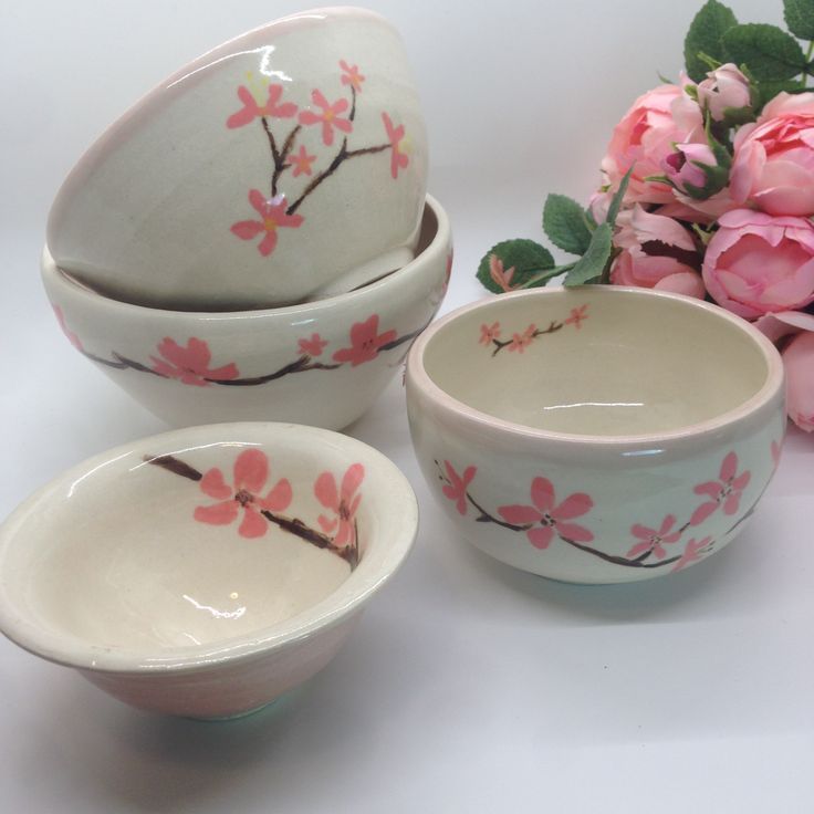 three bowls with flowers painted on them next to pink roses