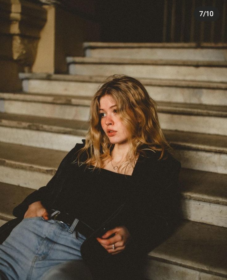 a woman sitting on some steps with her hands in her pockets