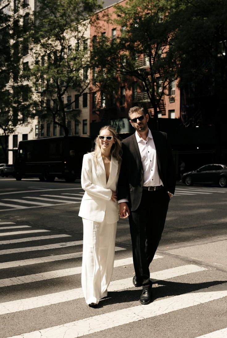 a man and woman are walking across the street holding hands while dressed in black and white