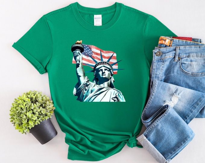 a green shirt with the statue of liberty on it next to jeans and a potted plant