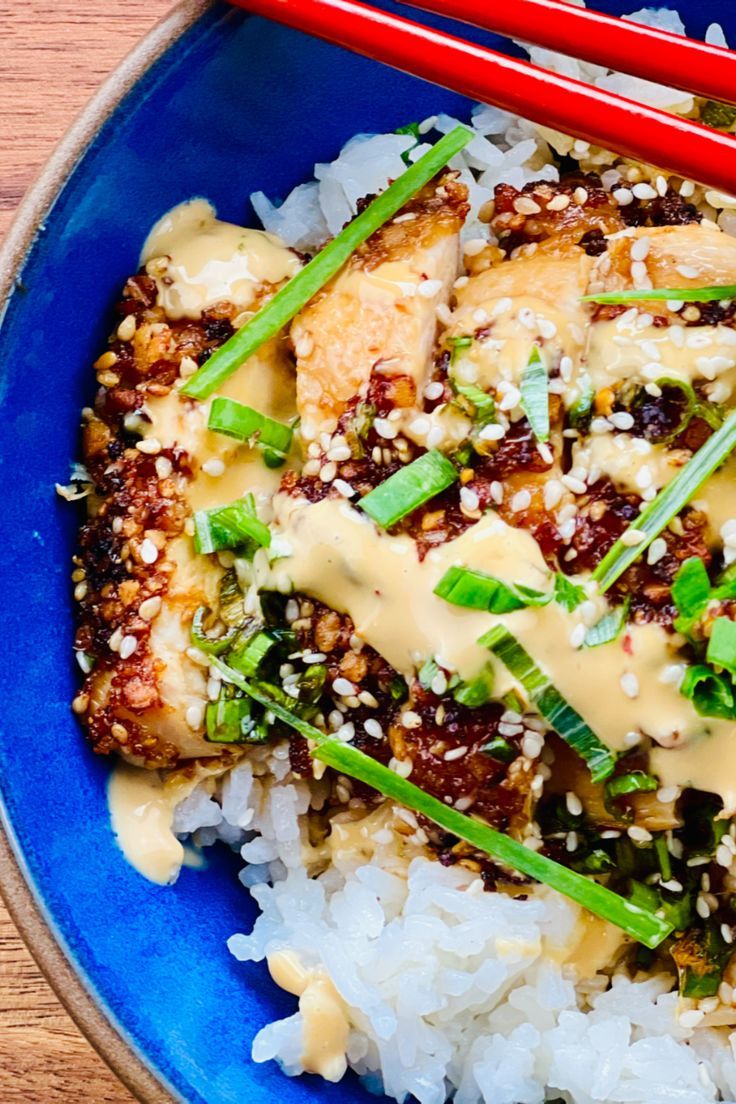 a blue plate topped with rice and meat covered in sauce next to chopsticks